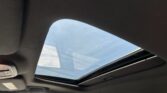 Inside a car cabin with the panoramic sunroof open, revealing blue sky and outside traffic nearby.