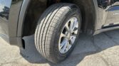 Front left wheel of a dark pickup truck, showing the tire and wheel inside the fender with some dirt in the wheel well