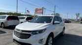 White Chevy SUV in a car dealership lot with EZ LOAN sign and an American flag in the background on a sunny day
