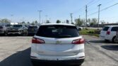 Rear view of a white Chevrolet Equinox in a parking lot with other cars and a clear blue sky above, power lines in the background.