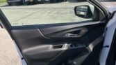 Open front passenger door with black interior panel; parking lot with many cars and dealership signs in the distance behind.