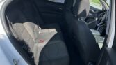 Interior of a gray fabric SUV shown from the open rear door, with front seats and rear bench visible; blue sky and parked cars seen outside.