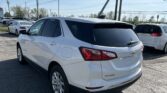White Chevrolet Equinox SUV parked in a lot with overhead power lines against a clear blue sky, foreground-focused rear three-quarter view of the vehicle.