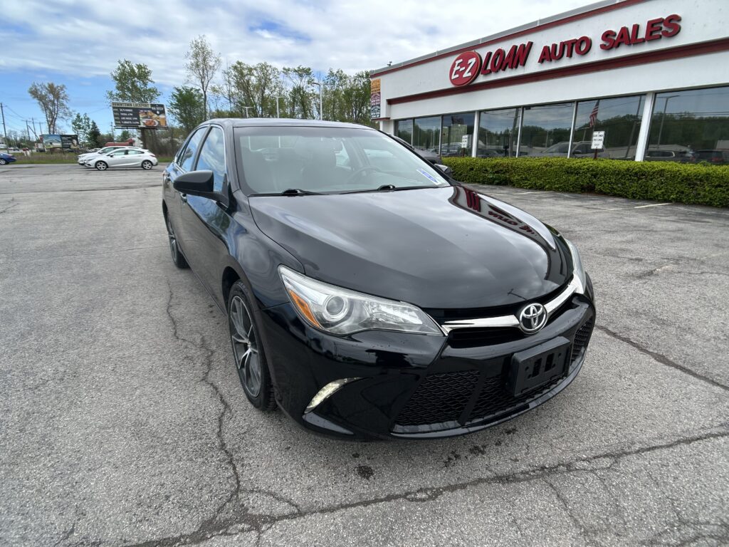 Front-right view of a black Toyota sedan parked in a lot outside EZ Loan Auto Sales storefronts.