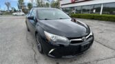 Front-right view of a black Toyota sedan parked in a lot outside EZ Loan Auto Sales storefronts.