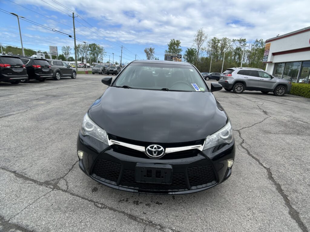 Front view of a black Toyota in a car dealership lot with other SUVs and a building on the right.