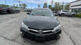Front view of a black Toyota in a car dealership lot with other SUVs and a building on the right.