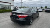 Black Toyota sedan in the foreground at a Toyota dealership lot with a showroom and many cars in the background.