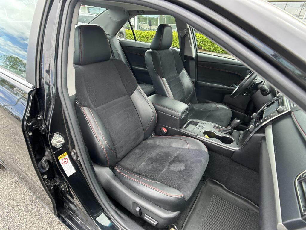 Open car door showing black cloth seats with red stitching in the front cabin, center console and steering wheel visible.