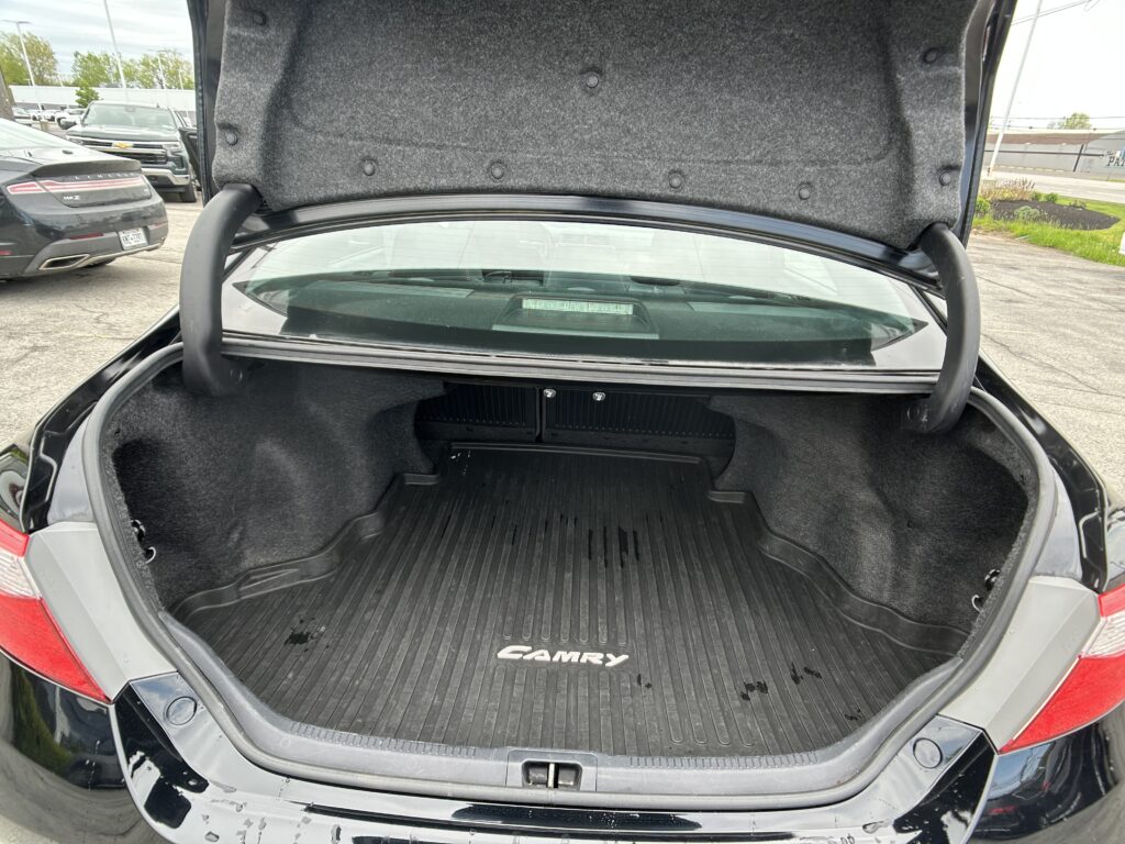 Open trunk of a black Toyota Camry showing a spacious cargo area with a ribbed mat and gray lining, in a dealership lot.