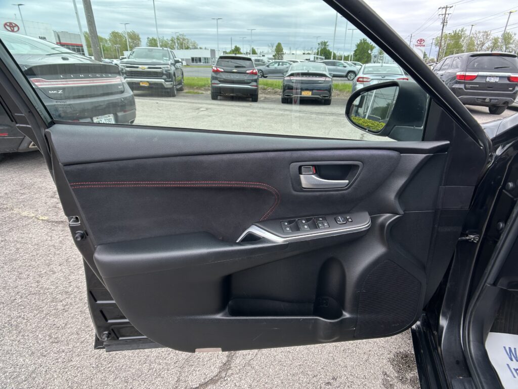 View from inside a car door, looking out at a dealership parking lot with several parked SUVs and sedans.