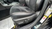 Front interior of a car showing black leather seats with red stitching, center console, and gear shifter beside the door frame with warning stickers.