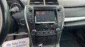 Interior view of a car dashboard: steering wheel on left, instrument cluster, central touchscreen, climate controls, and gear shifter with a paper flyer reading 'We Take Pride In Your Vehicle' visible on the left side of the seat.