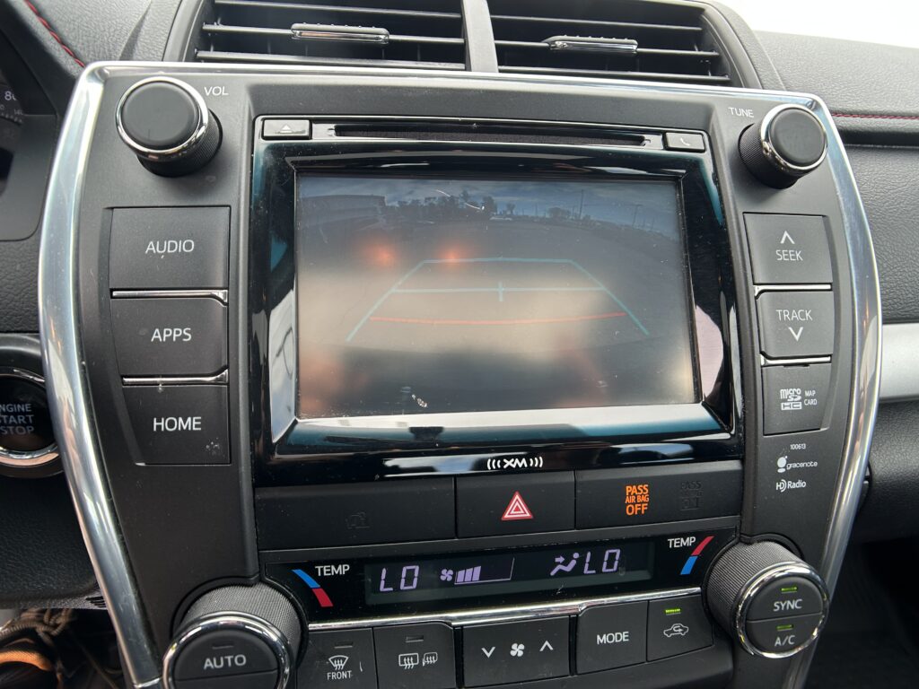 Car infotainment touchscreen surrounded by physical volume and tune knobs in a car dashboard.
