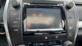 Car infotainment touchscreen surrounded by physical volume and tune knobs in a car dashboard.
