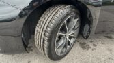 Close-up of a black car's front wheel with a treaded tire and alloy rim showing the fender above.