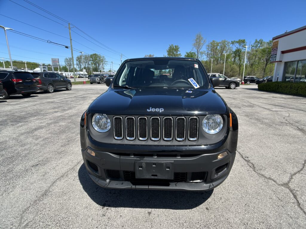 Front view of a black Jeep SUV in a car dealership lot under a clear blue sky, with other vehicles in the background.