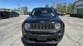 Front view of a black Jeep SUV in a car dealership lot under a clear blue sky, with other vehicles in the background.
