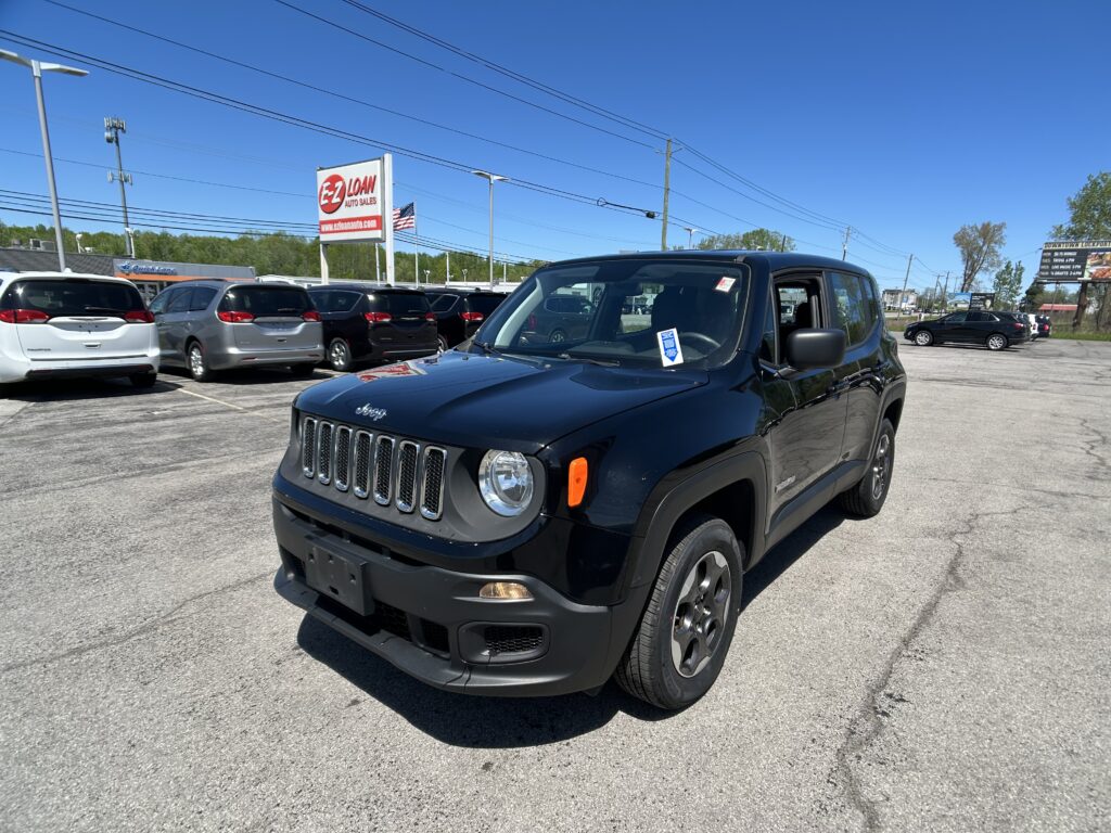Black Jeep in the foreground at a car dealership lot with other vehicles and a tall EZ LOAN sign against a clear blue sky.