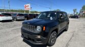 Black Jeep in the foreground at a car dealership lot with other vehicles and a tall EZ LOAN sign against a clear blue sky.