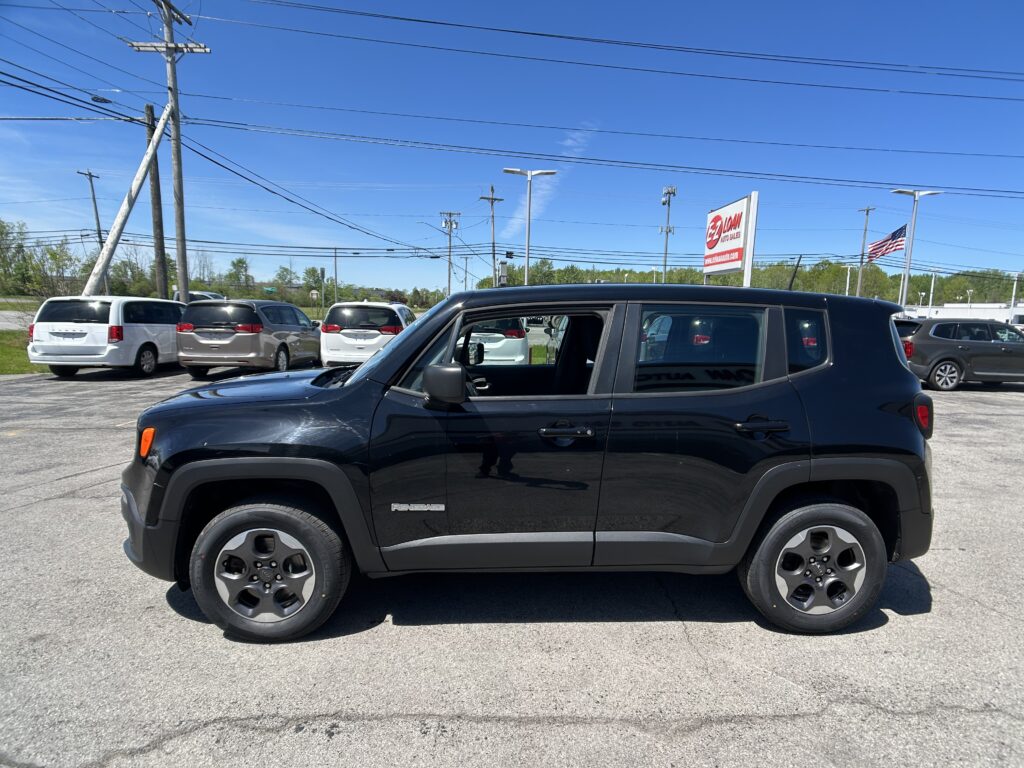 Black Jeep Renegade SUV in a dealership lot with white and silver minivans, power lines, and a tall dealership sign in the background.