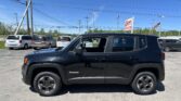 Black Jeep Renegade SUV in a dealership lot with white and silver minivans, power lines, and a tall dealership sign in the background.
