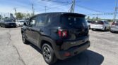 Rear view of a black Jeep Renegade in a sunny car dealership lot, with other cars and overhead power lines visible.