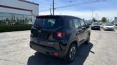 Rear view of a black Jeep SUV (Sport) in a dealership parking lot with other cars and a white building with red trim.