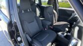 Front interior of a black SUV with two fabric seats, adjustable headrests, center console, and open door to outside parking lot.