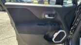 Interior of a car door panel with a silver door handle, window controls, and a speaker, viewable at a dealership lot outside the window.