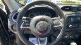 Front view of a Jeep steering wheel inside the car, with the instrument cluster and center console visible. Parking lot seen through the windshield.