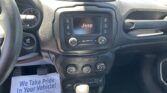 Interior view of a Jeep dashboard with the center touchscreen and climate controls; a paper flyer on the passenger seat reads 'We Take Pride In Your Vehicle'