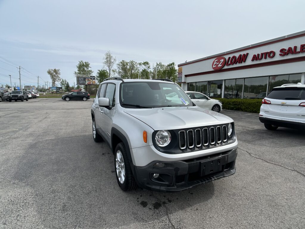 Silver Jeep in the foreground at a used car dealership, EZ Loan Auto Sales, with several cars in the lot.