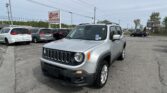 Front-right view of a silver Jeep SUV in a car dealership lot, with an E-Z LOAN Auto Sales sign and rows of minivans behind.
