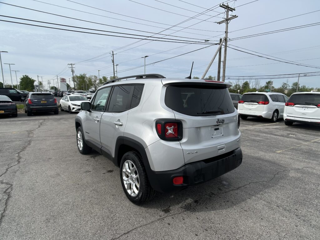 Silver Jeep SUV in a busy parking lot with many cars and tall power lines overhead in the background.