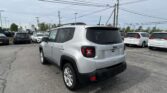 Silver Jeep SUV in a busy parking lot with many cars and tall power lines overhead in the background.