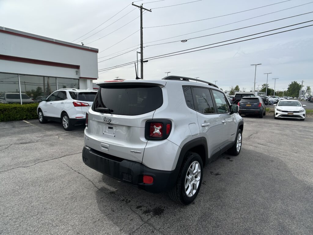 White Jeep SUV parked in a dealership lot, rear and right side visible with other cars in the background.