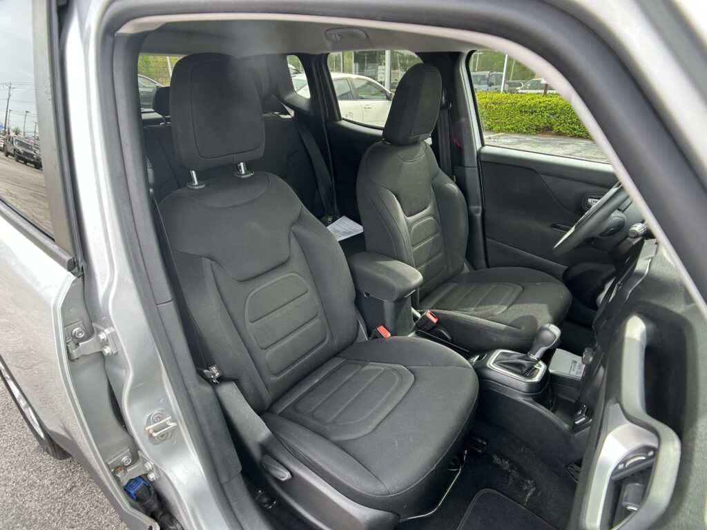 Front-seat view of a compact SUV with the driver's door open, showing black fabric seats and center console in a parking lot.