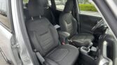 Front-seat view of a compact SUV with the driver's door open, showing black fabric seats and center console in a parking lot.