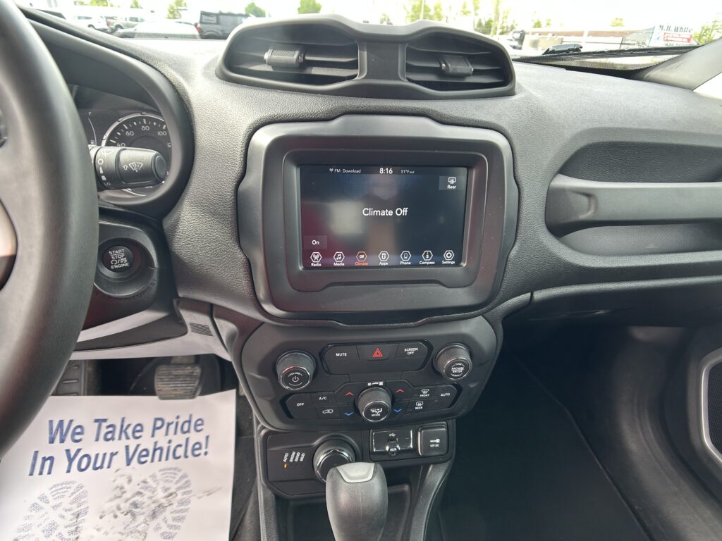 Interior of a car dashboard with center touchscreen displaying 'Climate Off', steering wheel on left, ignition/start button, and a paper flyer on the floor reading 'We Take Pride In Your Vehicle!'