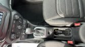 Inside a car showing the center console with gear shifter, climate control knobs, and black fabric seats nearby.
