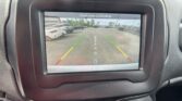 Car rearview camera display in a vehicle showing a parking lot with parked cars and green/yellow/red guiding lines, plus the message 'Check entire surroundings' on screen.
