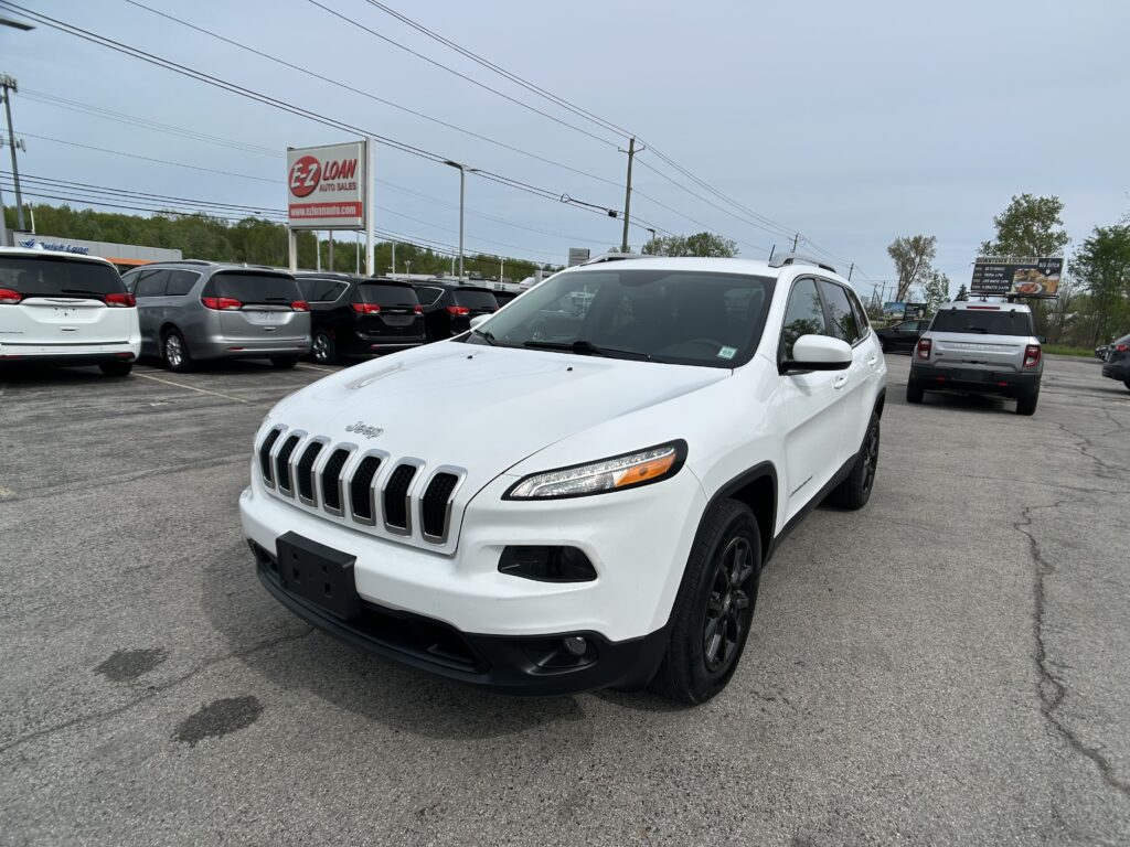 White Jeep SUV in the foreground at a car dealership lot, with rows of minivans and an EZ Loan Auto Sales sign in the background.