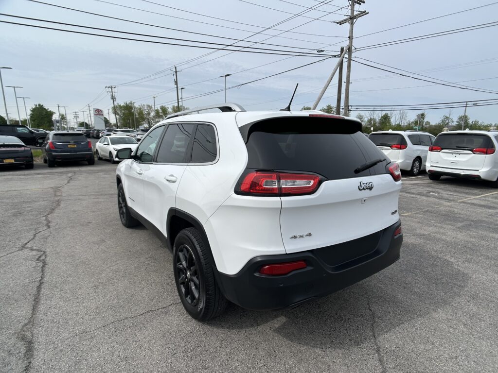 Rear three-quarter view of a white Jeep SUV in a crowded parking lot, with other cars and overhead power lines visible.