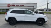 White Jeep Cherokee SUV in the foreground at an E-Z Loan Auto Sales lot with other cars and a Toyota dealership in the background.
