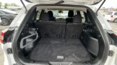 Open tailgate reveals spacious SUV cargo area with rear seats up and parking lot outside the vehicle windowed behind it.