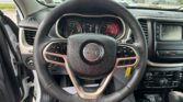 Driver's view of steering wheel and dashboard inside a Jeep, with instrument cluster and center console visible.