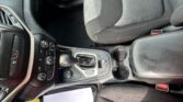 Interior of a car focusing on the center console, gear shift, and climate controls with papers on the floor mat nearby