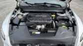 Front engine bay of a white car with the hood raised, featuring a black engine cover labeled 'MULTIAIR 2.4L' in a parking lot.🐱‍🏍