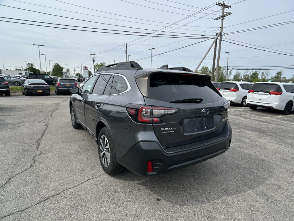 Rear view of a gray Subaru SUV in a crowded car dealership lot with power poles and overhead wires in the background.